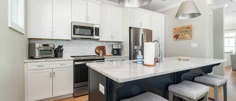 A modern kitchen with white cabinetry, stainless steel appliances, and a large island with bar stools.