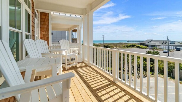Eine überdachte Veranda mit weißen Adirondack-Stühlen, ein Holzboden und Blick auf das Meer und den Pier.
