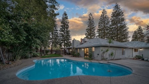 A backyard with a swimming pool, surrounded by trees and a house. - Pool| Game Room|3/2|Sleeps 10:Class Act in Fresno! (Fresno)