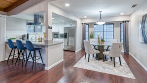 A modern kitchen with a central island, bar stools, and a dining area with a table and chairs. - Pool| Game Room|3/2|Sleeps 10:Class Act in Fresno! (Fresno)