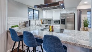 A modern kitchen with white cabinets, stainless steel appliances, and blue bar stools. - Pool| Game Room|3/2|Sleeps 10:Class Act in Fresno! (Fresno)