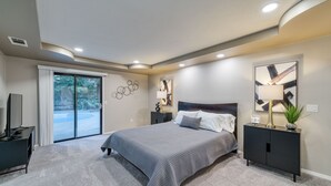 A bedroom with a large bed, a nightstand, a TV, and a sliding glass door leading to a balcony. - Pool| Game Room|3/2|Sleeps 10:Class Act in Fresno! (Fresno)