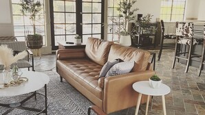 Ein geräumiges Wohnzimmer mit einer Ledersofa, gestreiften Sessel und einem runden Couchtisch, sowie einem Essbereich mit Tisch und Stühlen.