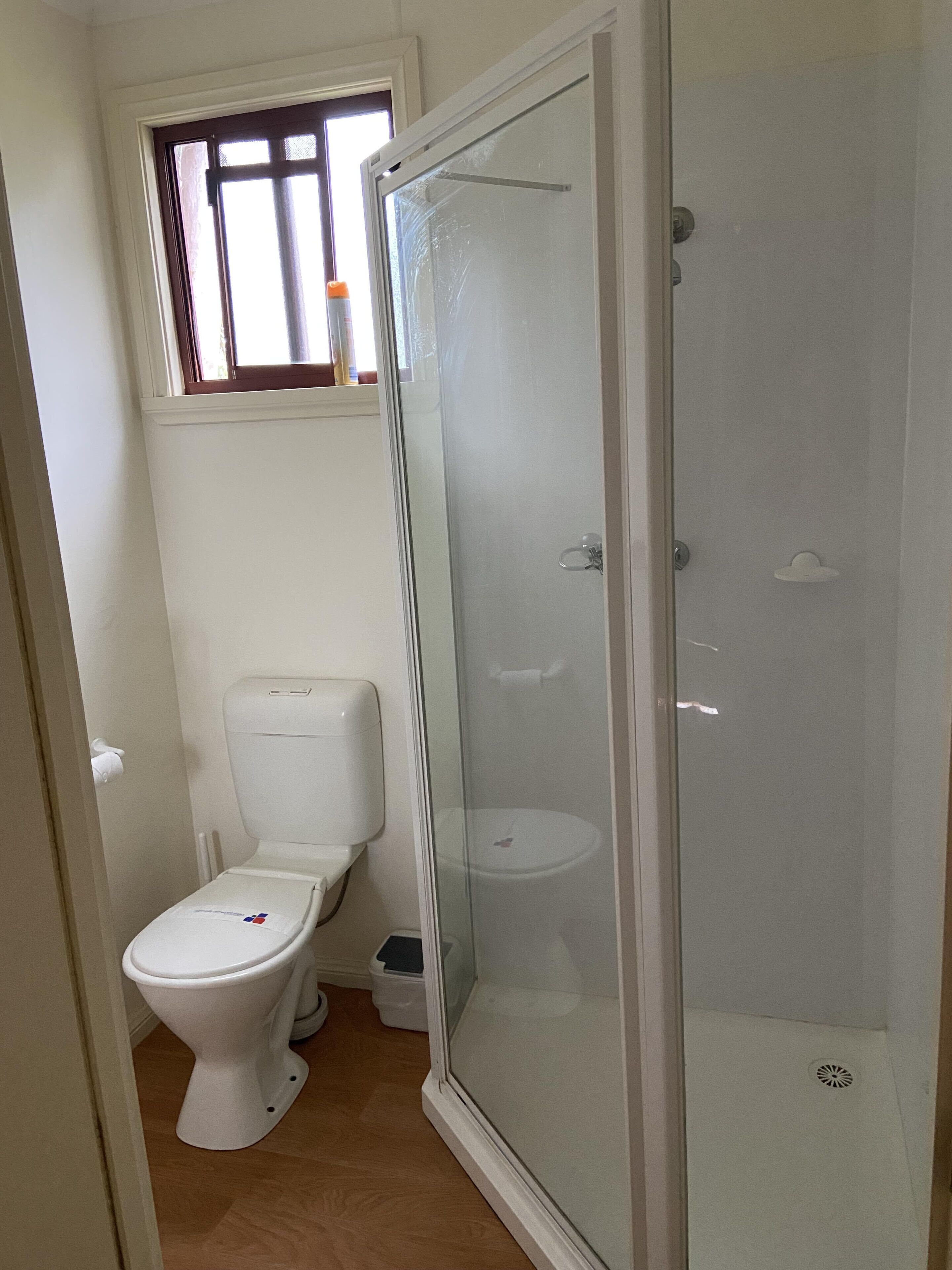 A bathroom with a toilet, a glass-enclosed shower, and a window above the toilet.