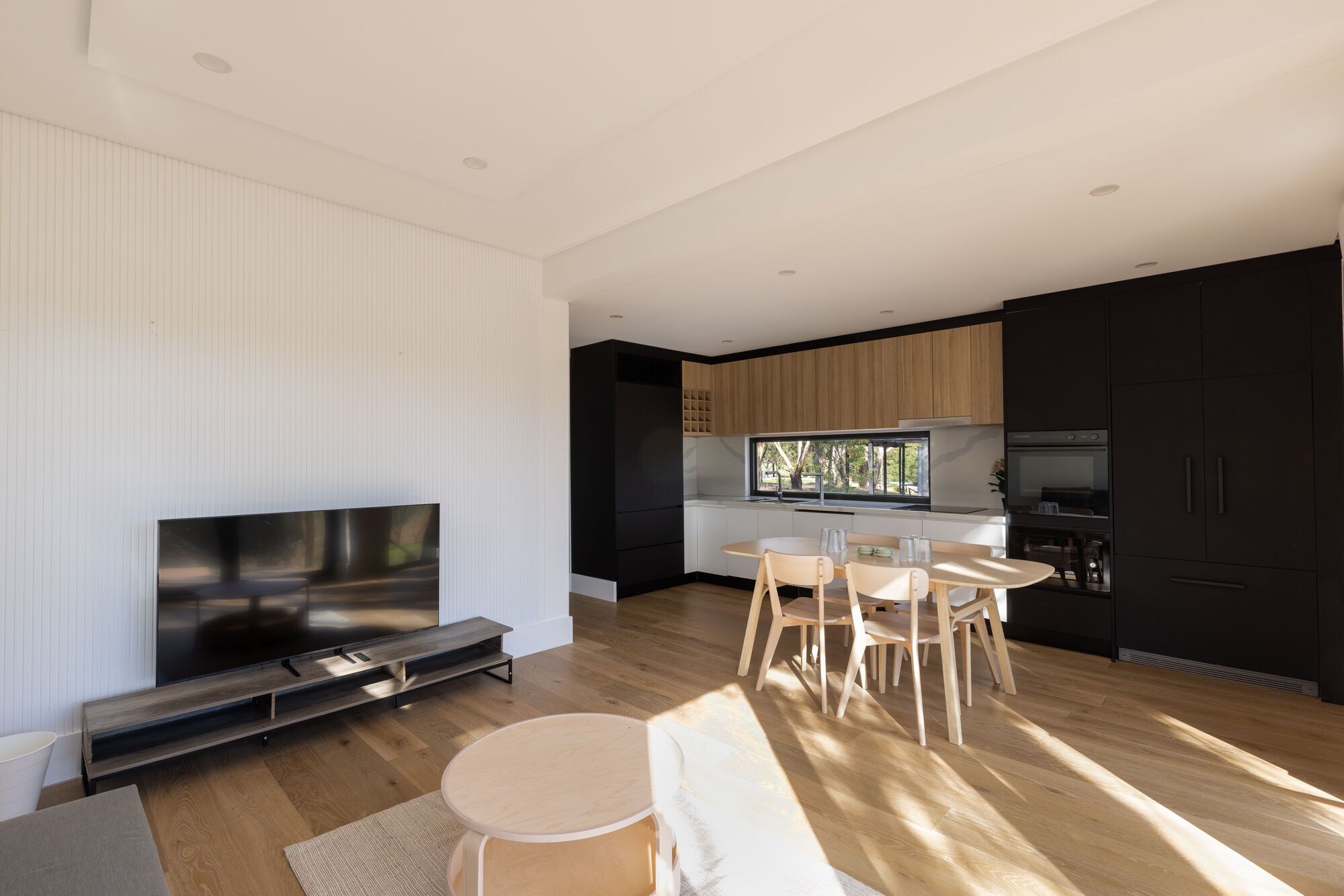 A modern kitchen with wooden cabinets, a dining area with a table and chairs, and a TV on a stand.