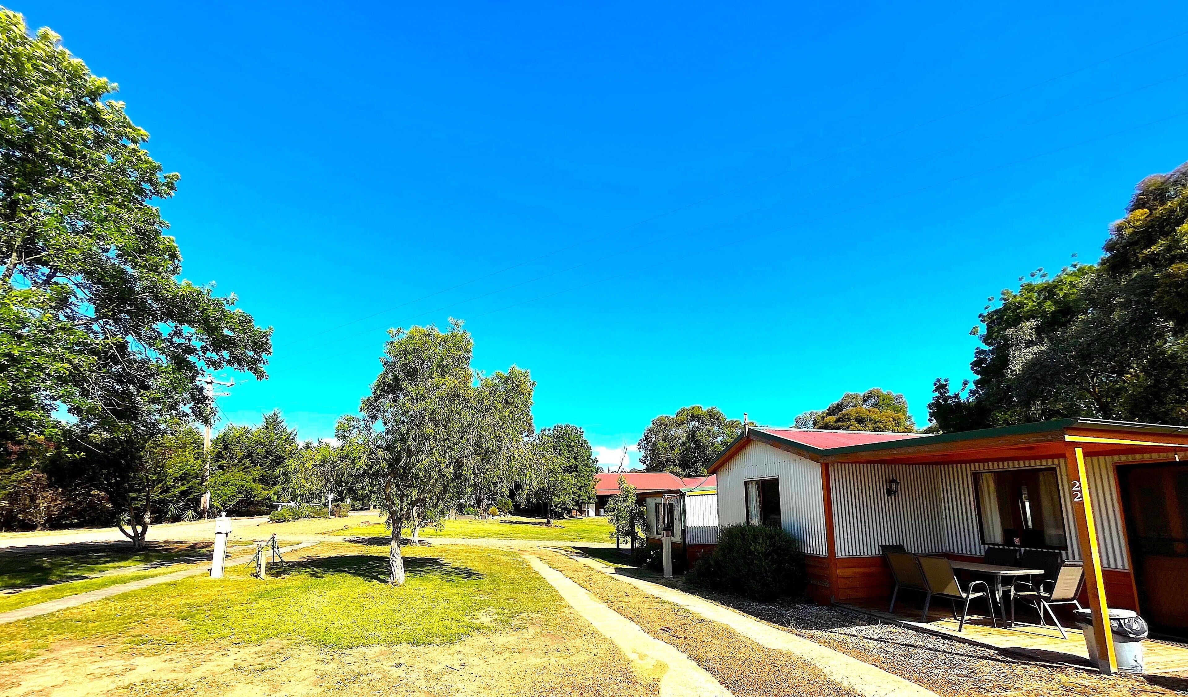 Un camping con un área de comedor cubierta, mesas de picnic y un pequeño edificio con techo rojo.