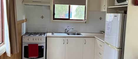 A compact kitchen with a gas stove, oven, sink, and a microwave.