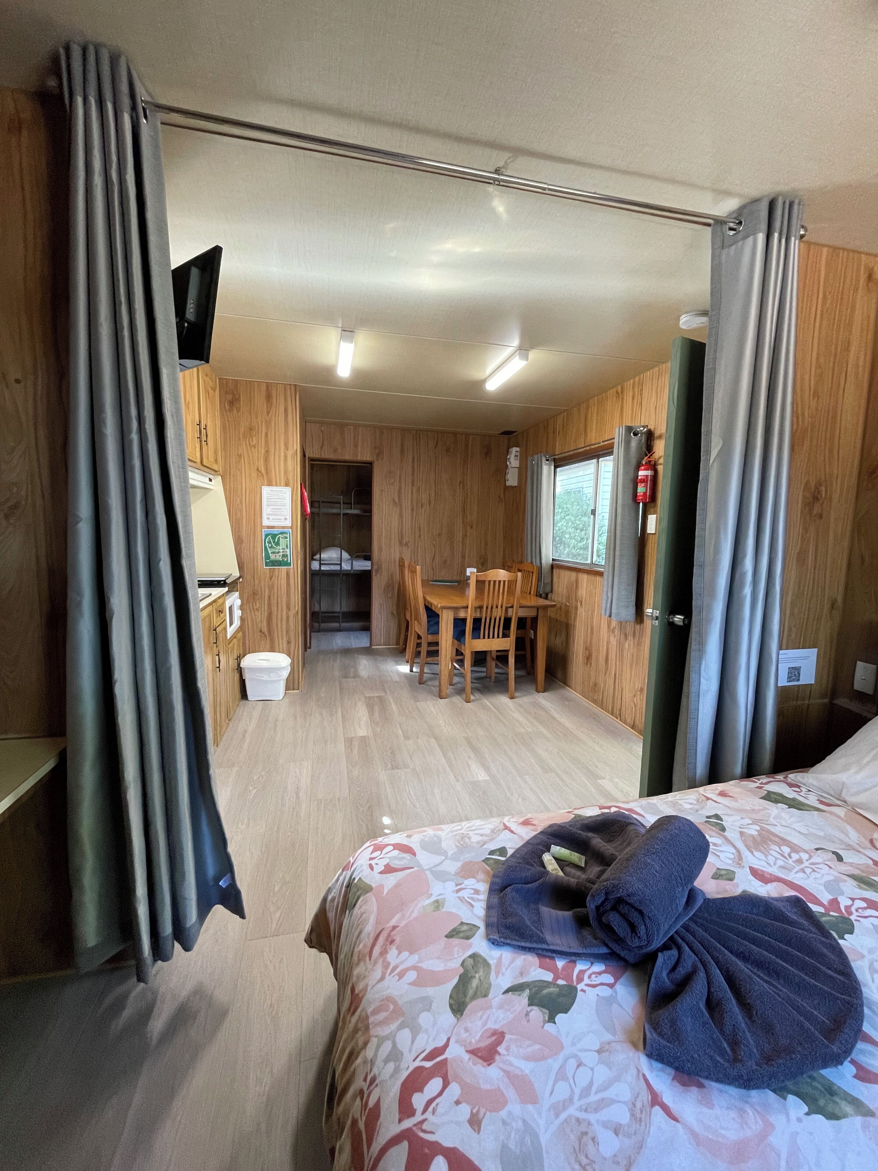 A room with a bed, a table, and chairs, wooden walls, a window, and a door.