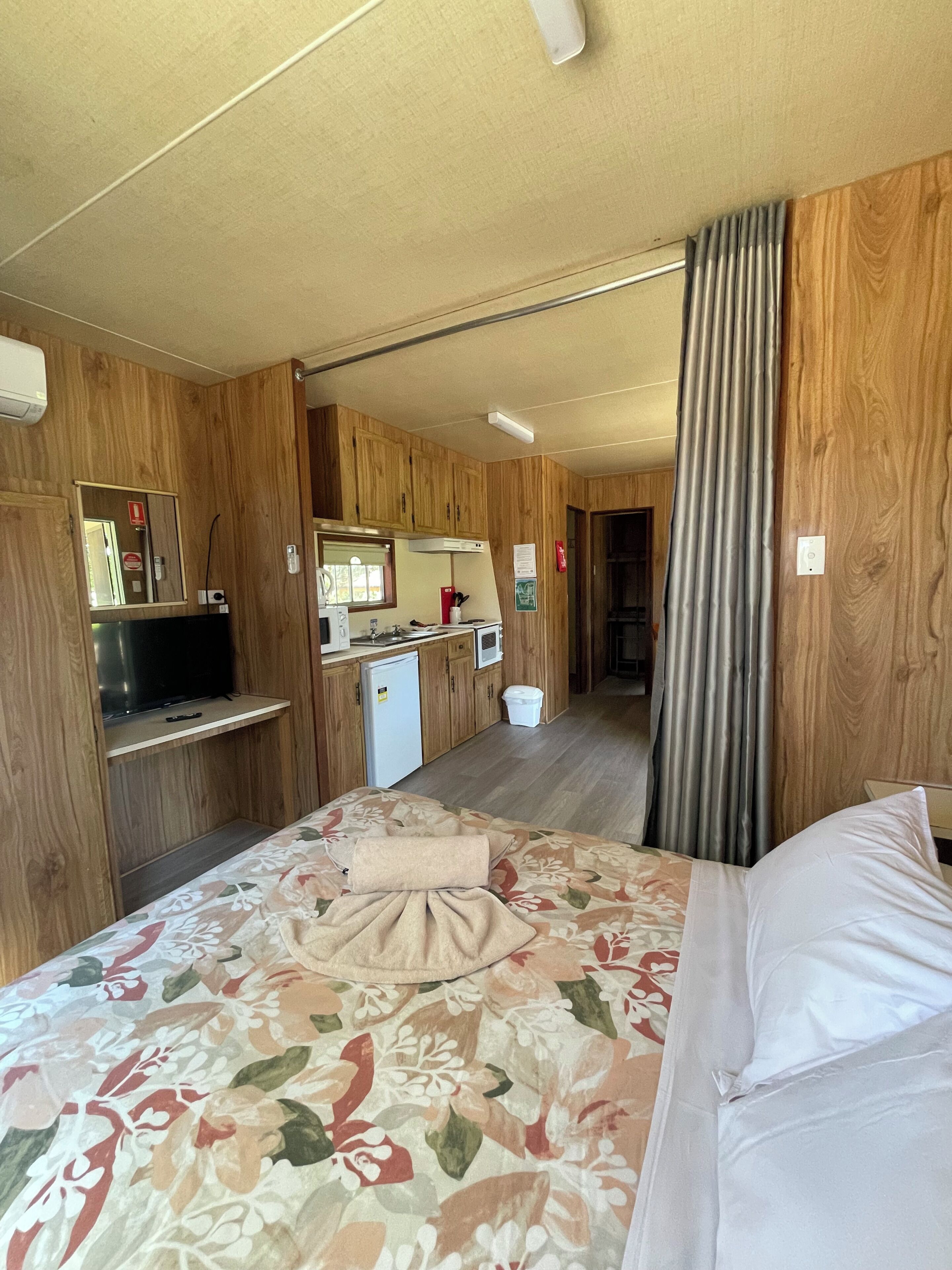 Une chambre avec un lit, une petite kitchenette, un miroir et un téléviseur.