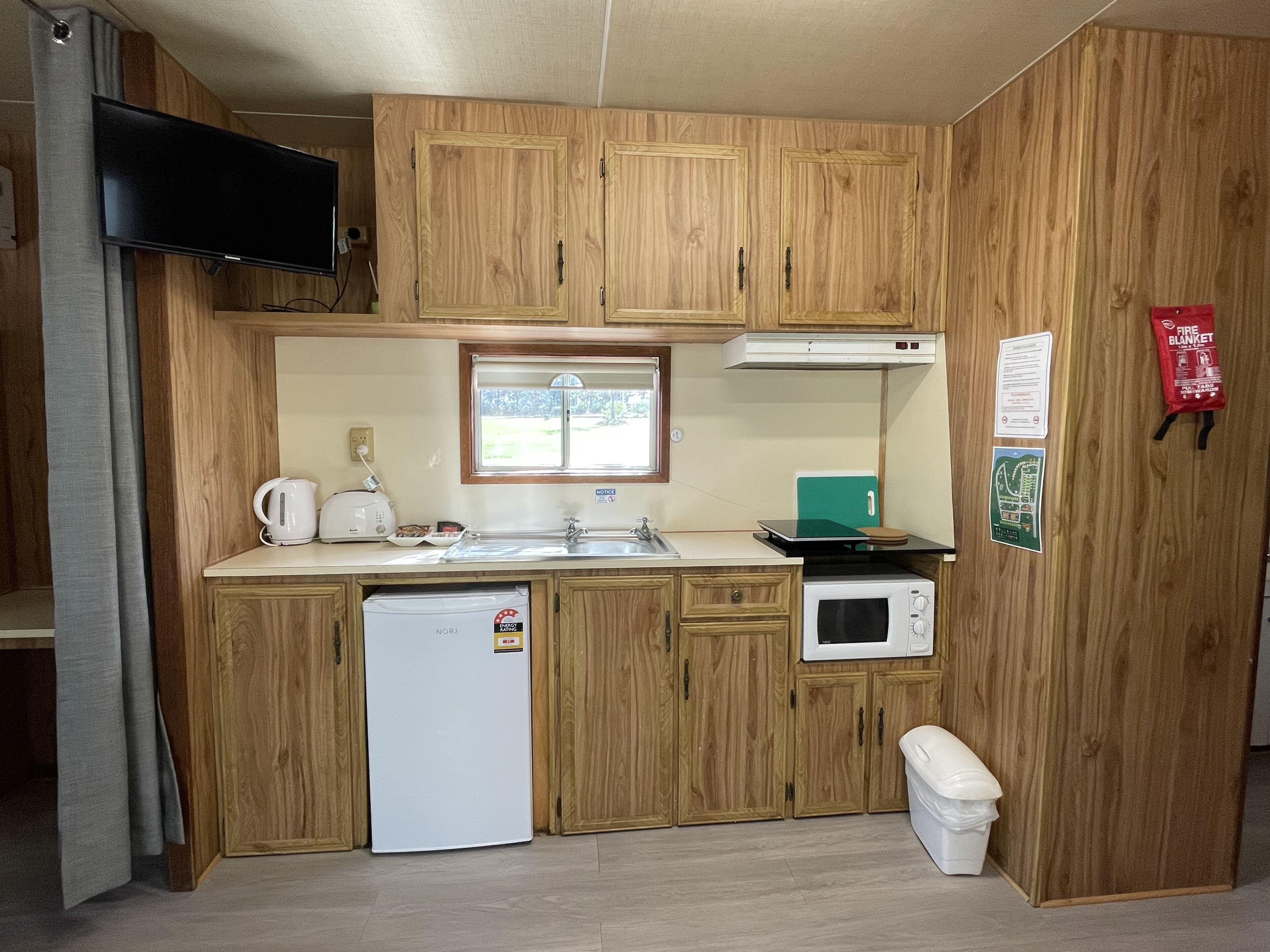 Une cuisine compacte avec des meubles en bois, un four à micro-ondes encastré, un lave-vaisselle et une fenêtre au-dessus de l’évier.