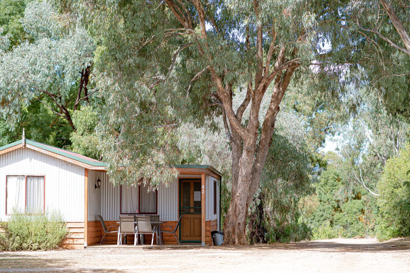 A small cabin with a wooden exterior, a single door, and a small porch area with a table and chairs.