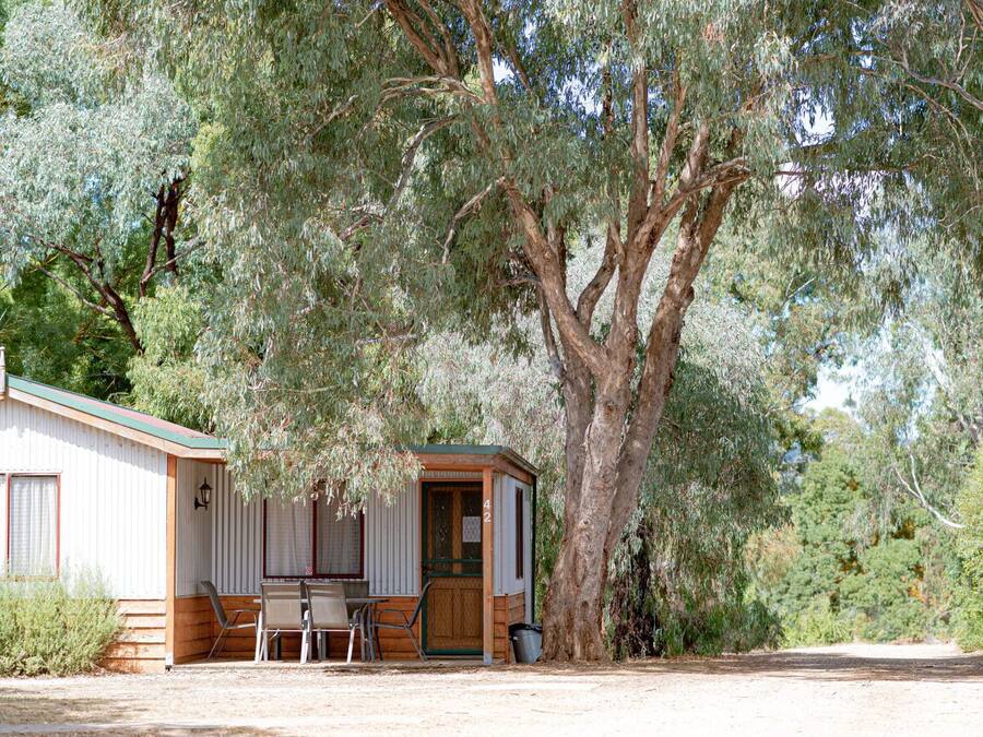 A small cabin with a wooden exterior, a single door, and a small porch area with a table and chairs.