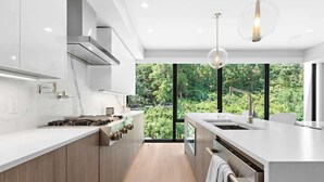 A modern kitchen with a large island, stainless steel appliances, and a view of greenery through large windows.