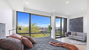 A modern bedroom with a large bed, a sofa, and a view of the city through large windows.
