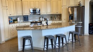 Una cocina con armarios blancos, un refrigerador de acero inoxidable, un microondas y una isla grande con taburetes de bar.