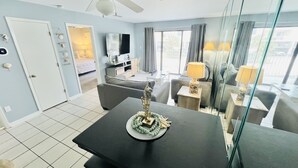 Een moderne woonkamer met een plafondventilator, een flatscreen televisie en een eethoek met een tafel en stoelen.