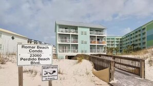 Een appartementencomplex aan het strand met meerdere balkons en een bord met een beveiligingsmelding.