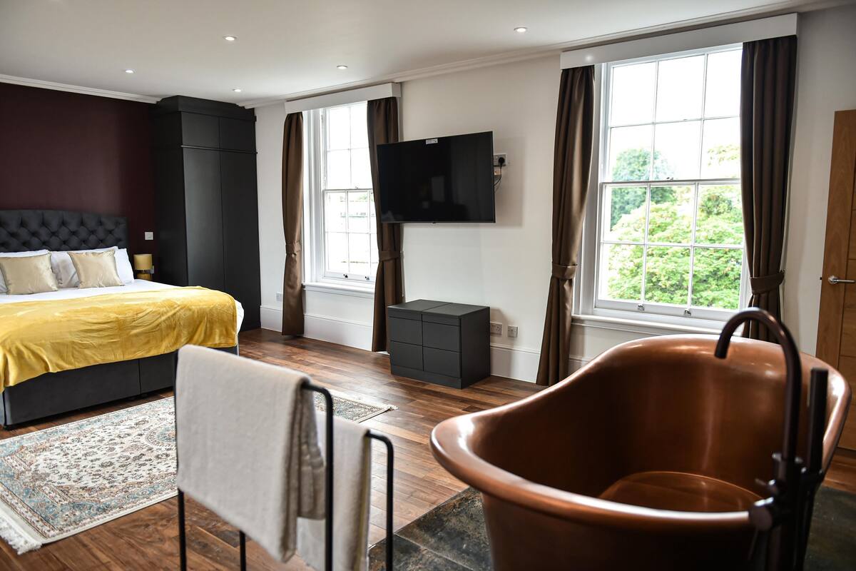 A modern bedroom with a bed, a television, a large window, and a bathroom with a bathtub.