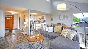 Ein modernes Wohnzimmer mit grauem Sofa, Couchtisch aus Holz und einem Essbereich mit Holztisch und Stühlen.