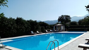 Ein rechteckiger Swimmingpool mit klarem, blauem Wasser, umgeben von Liegestühlen und einer Laube.