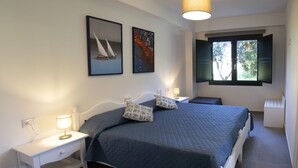 Ein Schlafzimmer mit einem Bett, zwei Nachttischen, einem Fenster mit Fensterläden und zwei an der Wand befestigten Bildern.