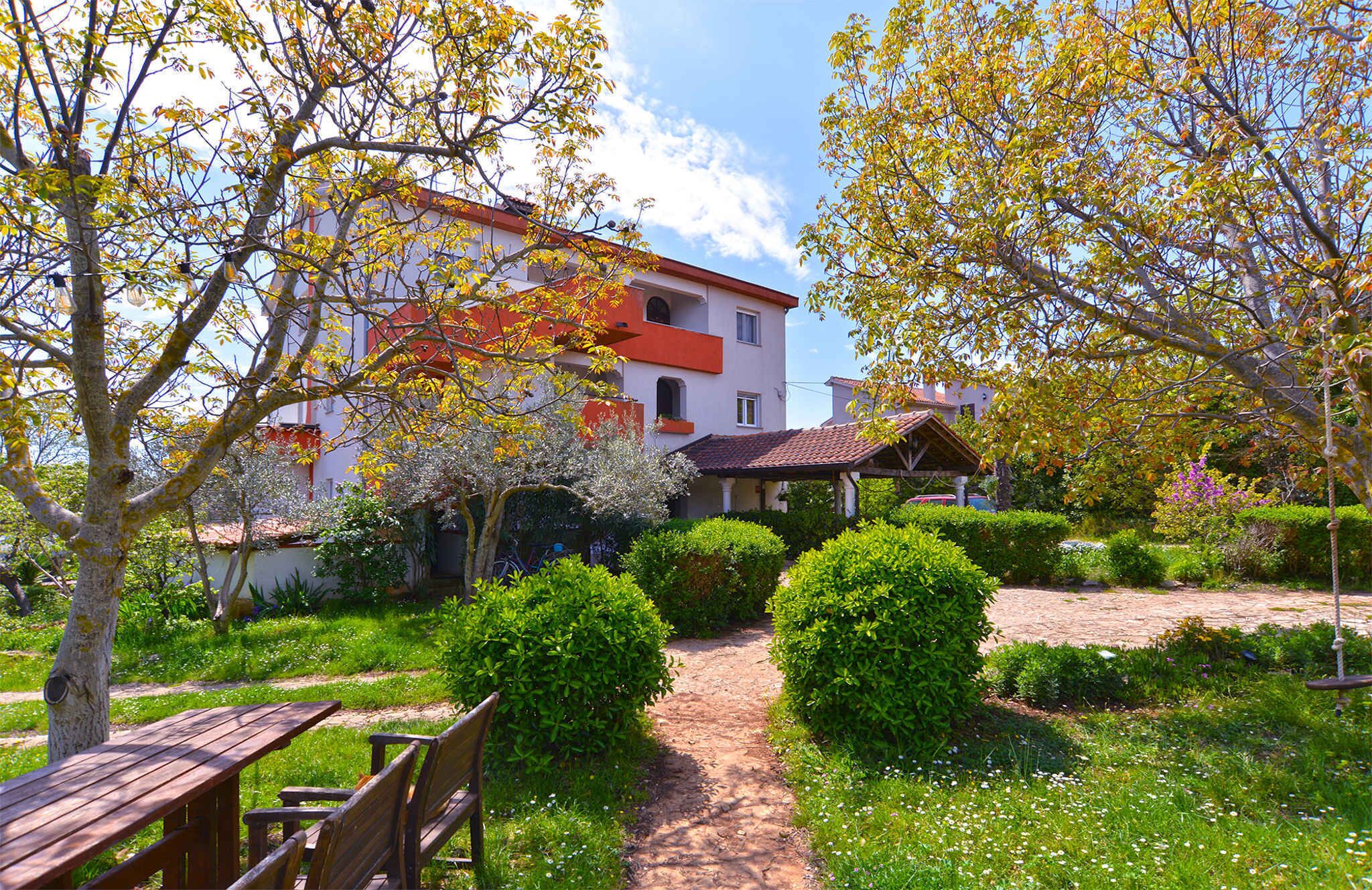 A garden path leading to a building with a red roof and white walls, surrounded by lush greenery and trees with autumn leaves.