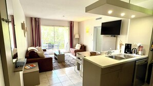 Een moderne keuken met een centraal eiland, een eethoek met een tafel en stoelen, een bank en een aan de muur bevestigde televisie.