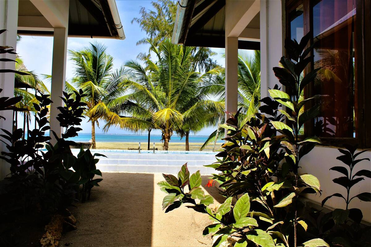 A covered outdoor area with a view of the beach and palm trees.