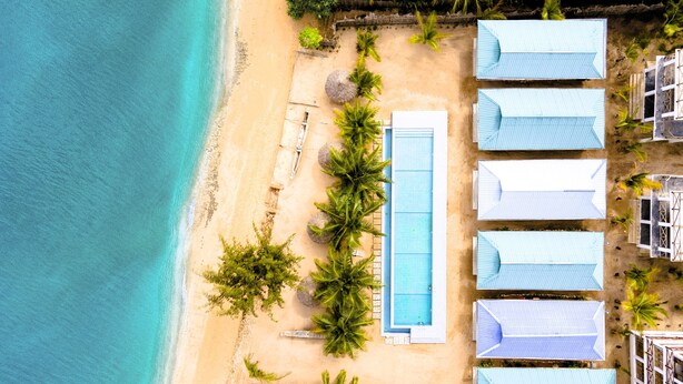 An aerial view of a beachside resort with a swimming pool, palm trees, and beach huts. - Asante Sana Beachfront Hotel (Fukuchani)