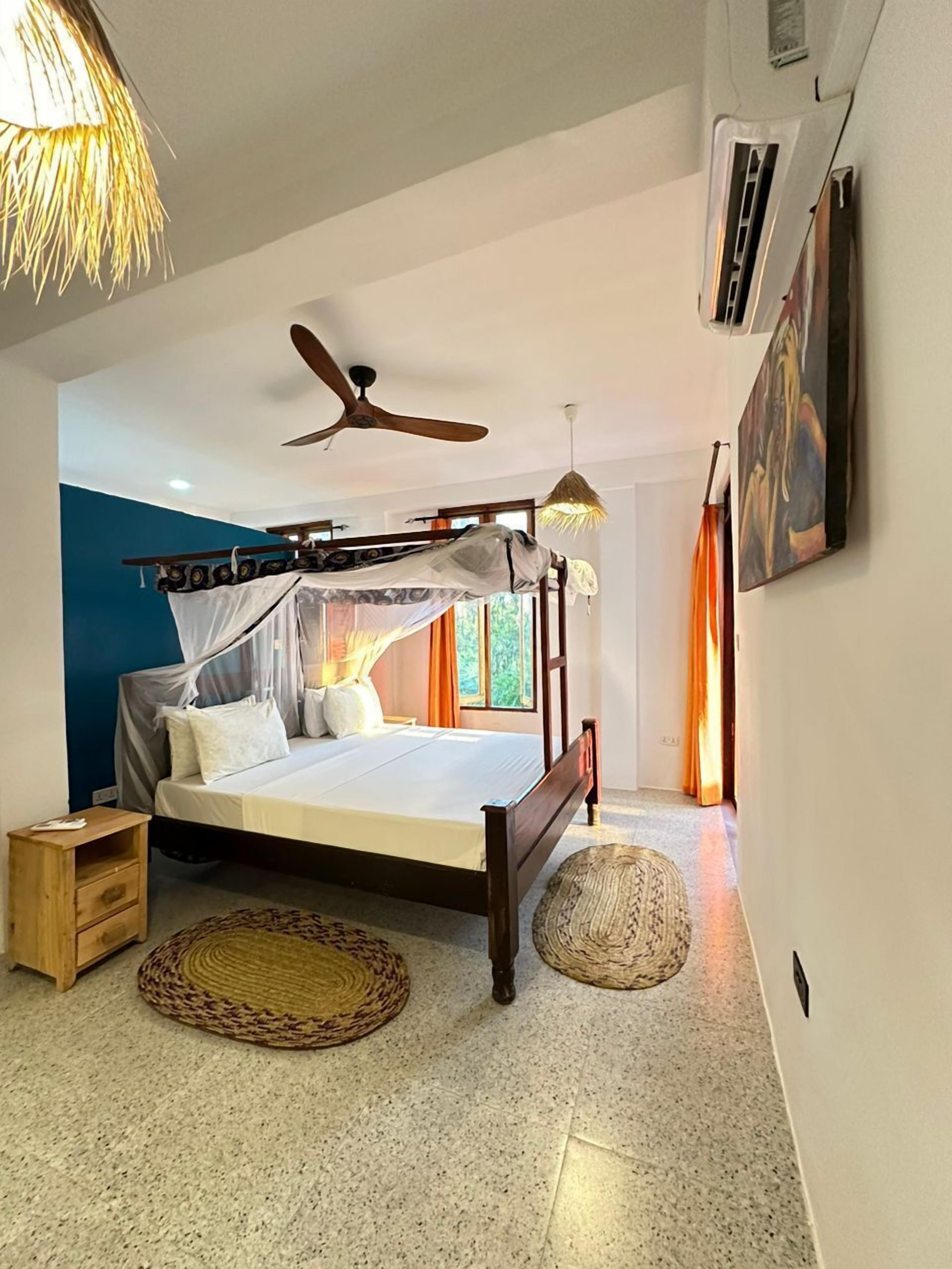 Un dormitorio con una cama, ventilador de techo, un cuadro y una ventana.
