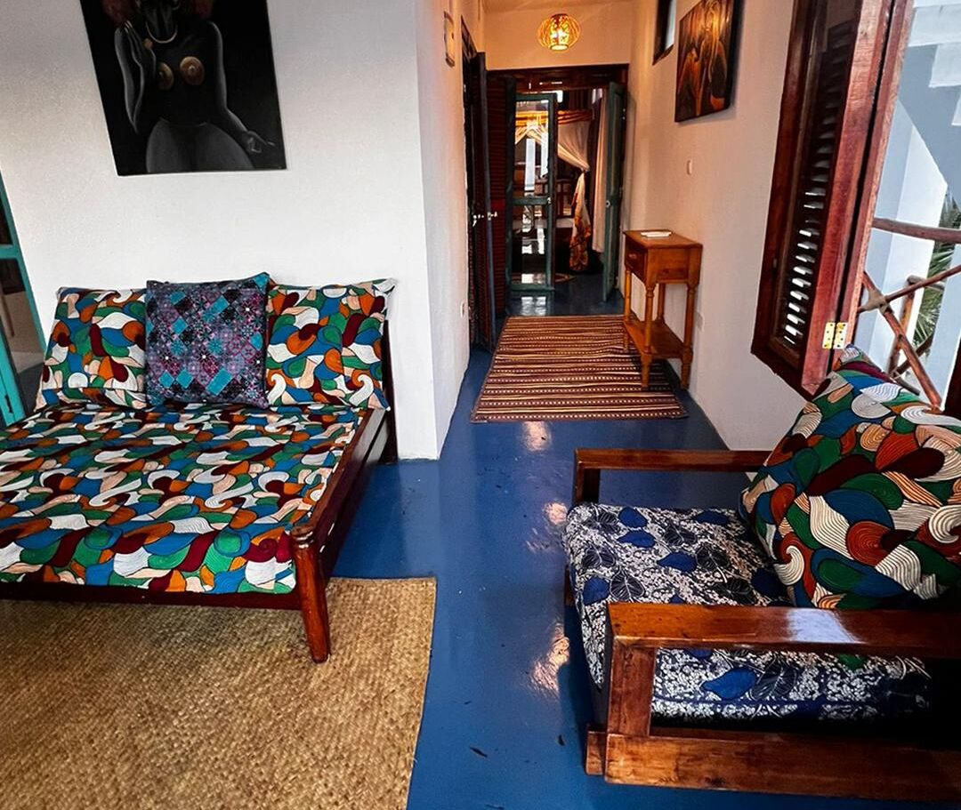 A hallway with a blue floor leading to a bedroom with a bed and a wooden chair.