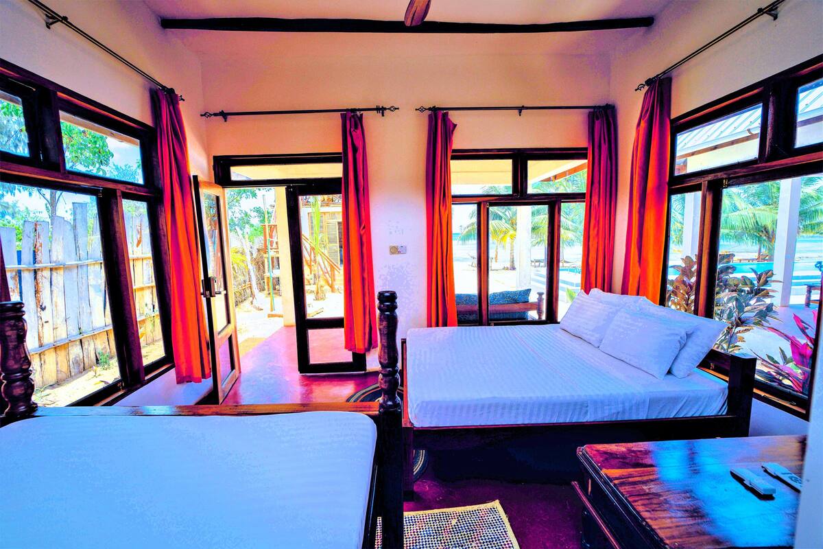 A room with two beds, large windows, and curtains.