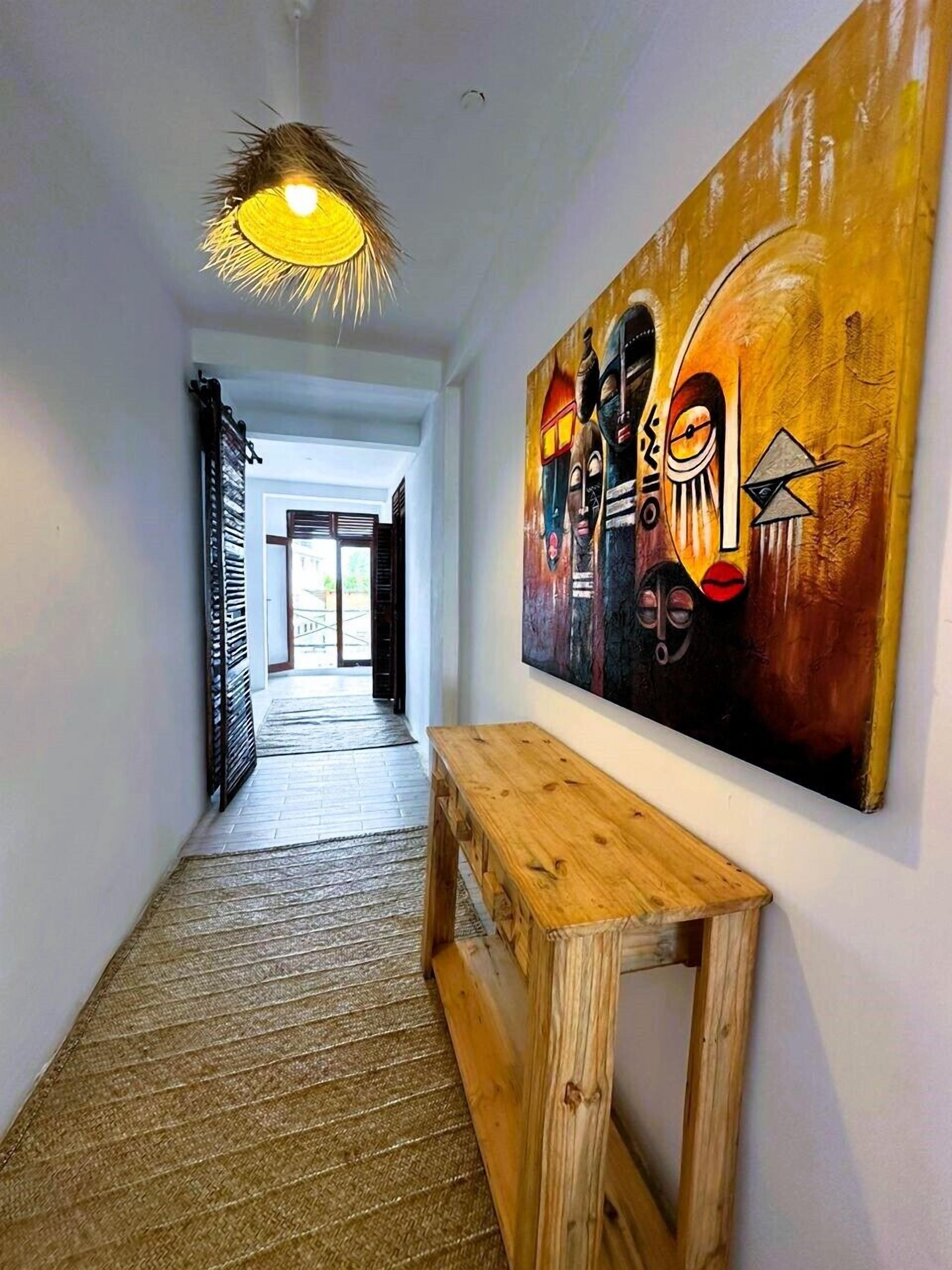 Un pasillo con un banco de madera, un cuadro abstracto de gran tamaño en la pared y una lámpara colgante.