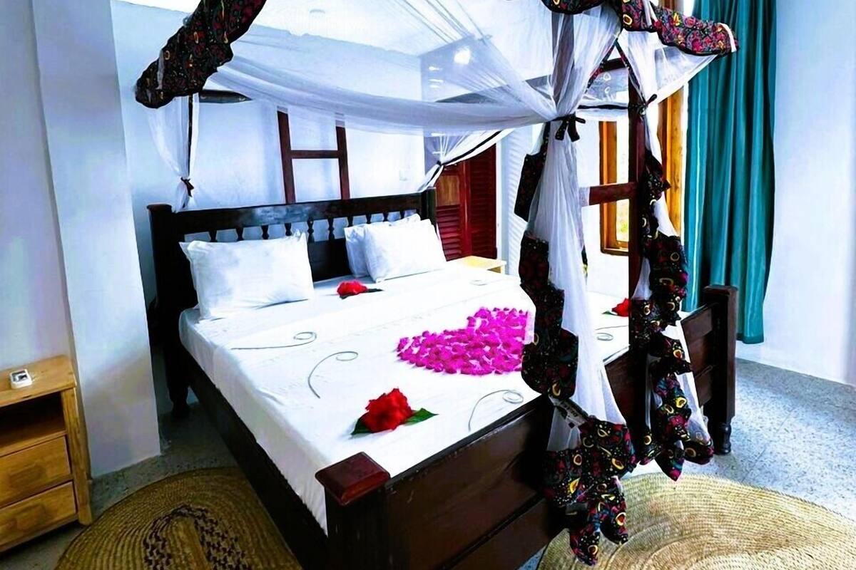A four-poster canopy bed with a wooden headboard, white bedding, and decorative pillows.