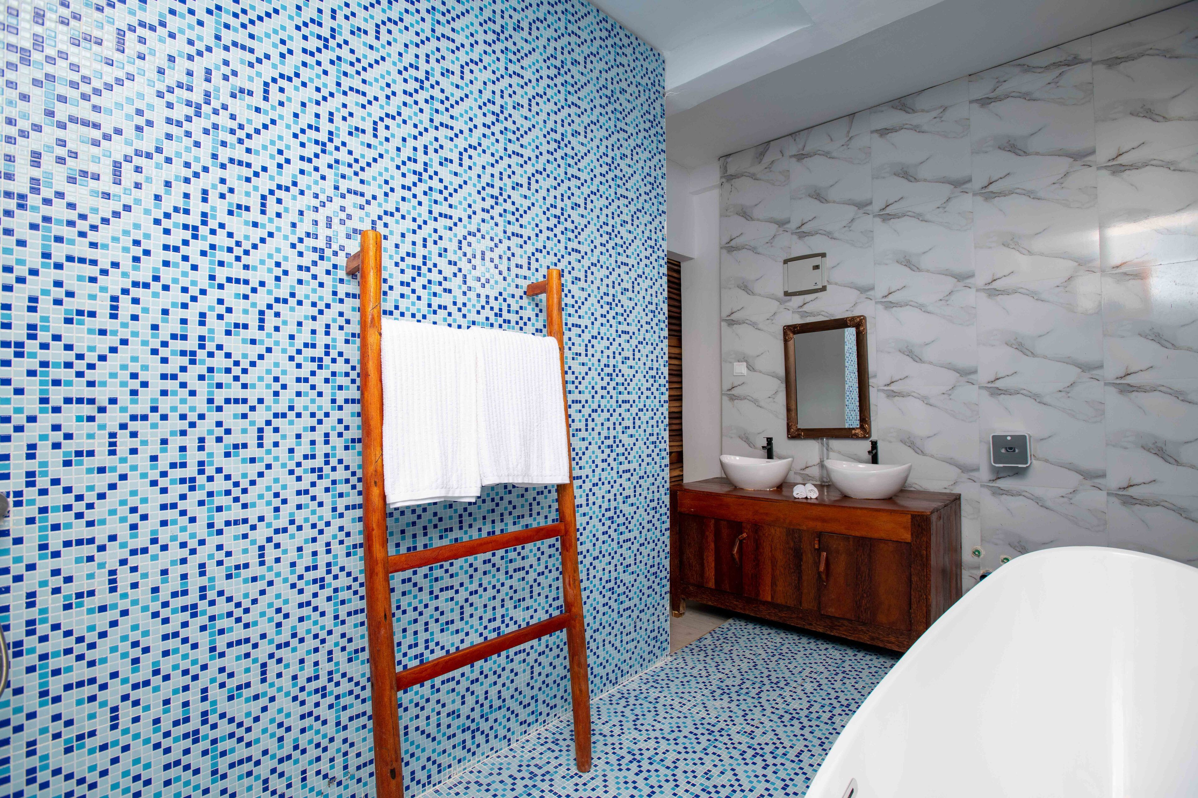 A bathroom with mosaic tile walls, a wooden ladder, a white sink, and a bathtub.