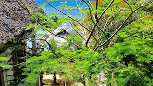 A lush garden with a thatched roof structure and a view of the ocean. - Asante Sana Beachfront Hotel (Fukuchani)
