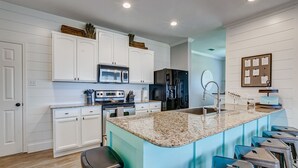 A modern kitchen with white cabinetry, a granite countertop, and a built-in island with bar stools. - Savings Alert! Pet-Friendly: Spacious, Fenced Retreat, Views! Games!  Sleeps 14 (Crystal Beach)