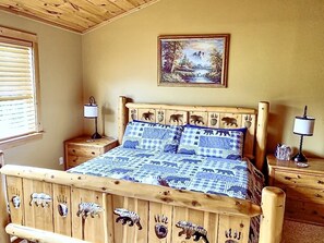 Una cama de madera con estampados de animales, un cuadro de un paisaje y dos lámparas de noche.