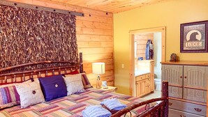 Tunnelmallinen huone, jossa on puinen sängynpääty, värikäs peitto sängyllä, yöpöytä lampun kanssa ja lipasto, jossa on kyltti, jossa lukee ”The Black Bear Lodge”.