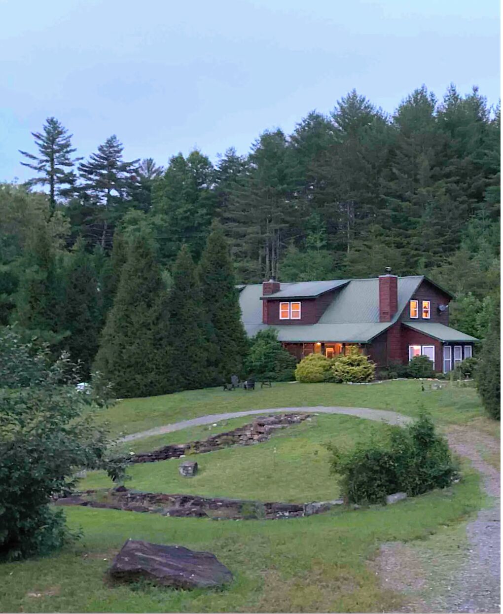 A two-story house with a stone foundation, surrounded by a well-maintained lawn and a stone wall.