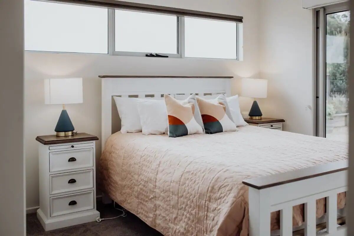 A bedroom with a bed, two bedside tables, a window, and a view of greenery outside.