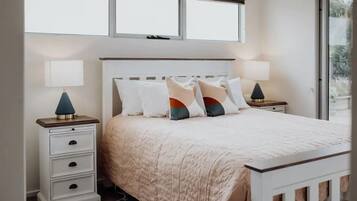 A bedroom with a bed, two bedside tables, a window, and a view of greenery outside.