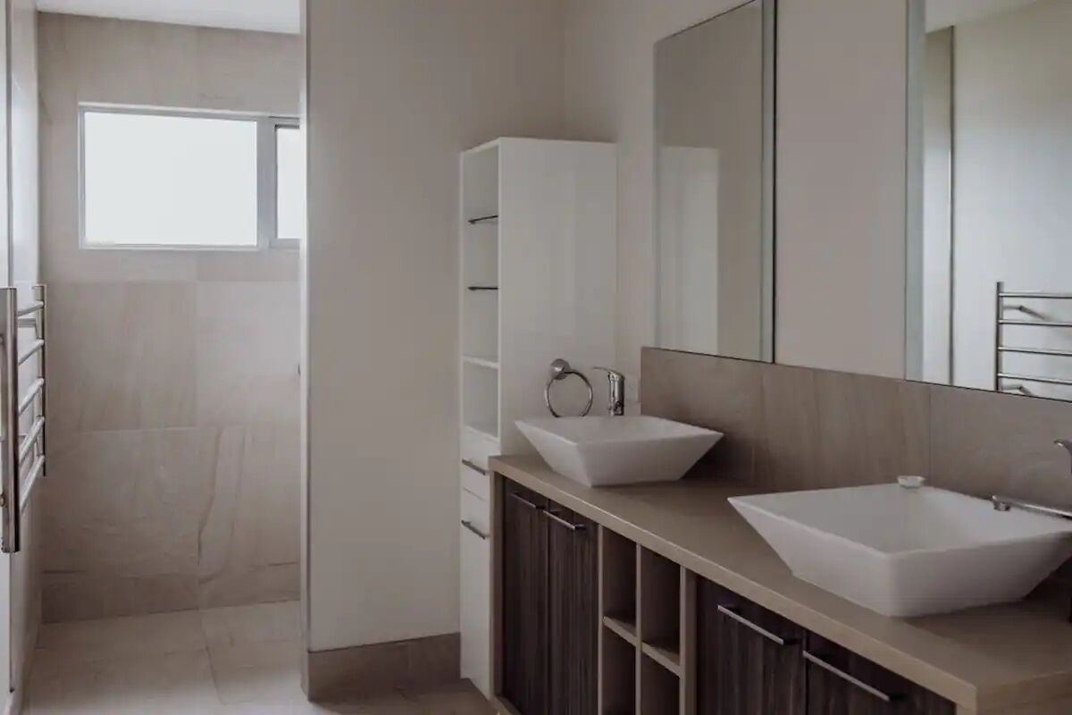 Ein modernes Badezimmer mit zwei Waschbecken, einem großen Spiegel und einer begehbaren Dusche.