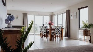 Un amplio salón con mesa y sillas de comedor, ventanas grandes y vistas al exterior.