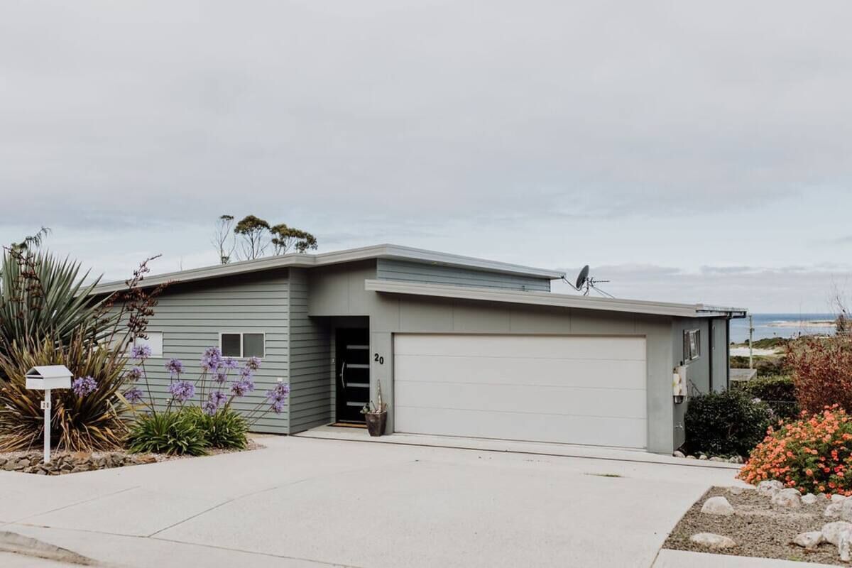 A modern single-story house with a garage, surrounded by landscaped gardens and a view of the ocean.