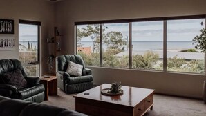 Una sala de estar moderna con un amplio ventanal que ofrece vistas al mar y al verdor.