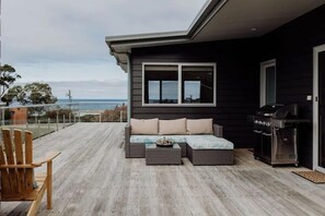 A deck with a sofa, a grill, and a chair. - BEST BICHENO ESCAPE - GARDENS & REDBILL BEACH (Glamorgan-Spring Bay)
