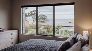 Un dormitorio con un amplio ventanal que ofrece vistas al mar y al verdor.