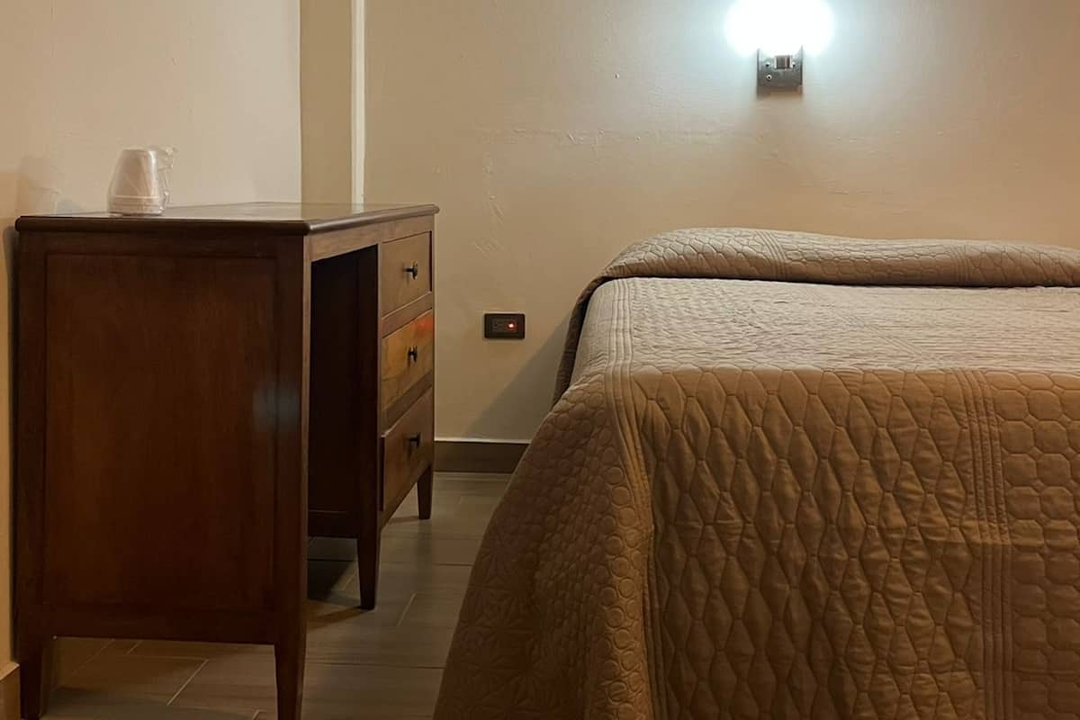 Quarto com cama, cómoda de madeira e luminária fixada na parede.