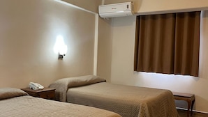 Habitación de hotel con dos camas, una mesita de noche con teléfono, aire acondicionado de pared y una ventana con cortinas.